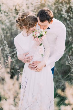 Yakışıklı damat yavaşça çiçek açan bahar bahçesinde buket tutarak gelin geri tutar