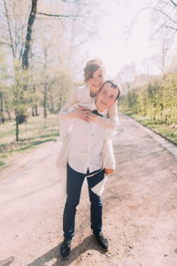 Damat gülümseyen güzel sarışın gelini arka açık havada bahar parkta taşır