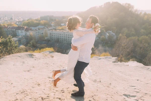 Ritratto di sorridente coppia di sposi danzanti in cima alla collina, città e cielo sfondo — Foto Stock