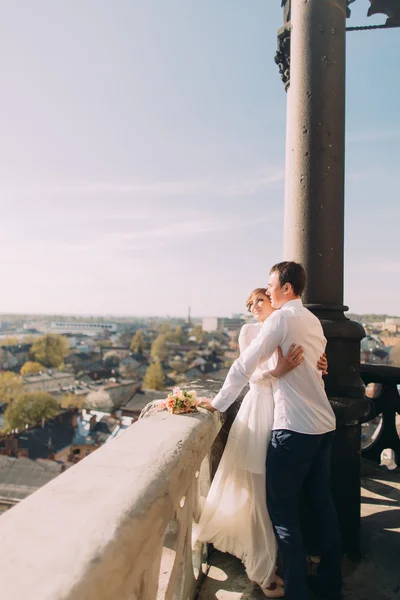 Красива весільна пара молодята обіймаються на балконі з видом на старе місто — стокове фото