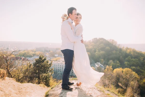 Bella coppia di sposi che si abbracciano contro le montagne sullo sfondo della città — Foto Stock