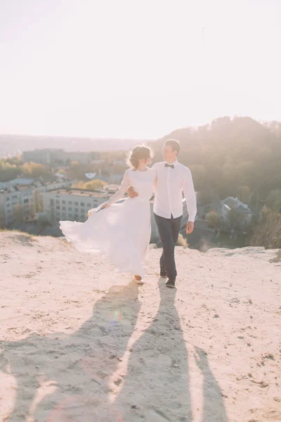 Красивый жених в белой рубашке и невеста в свадебном платье прогуливаясь на фоне города — стоковое фото