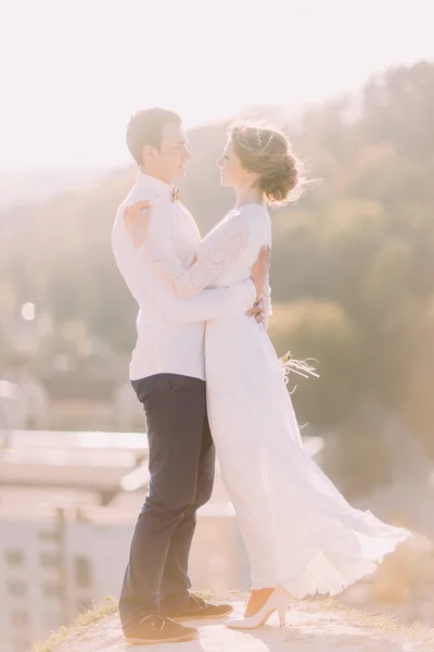 Primo piano di una romantica coppia di sposi che si guardano e si abbracciano con le braccia sullo sfondo della città — Foto Stock