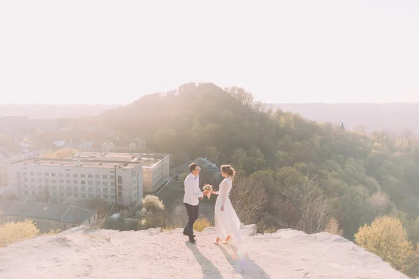 Улыбающиеся молодая невеста и жених держатся за руки вместе с букетом — стоковое фото