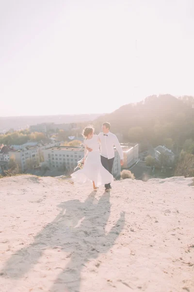 Όμορφος γαμπρός σε λευκό πουκάμισο και νύφη φορώντας νυφικό φόρεμα περπάτημα στο φόντο της πόλης — Φωτογραφία Αρχείου