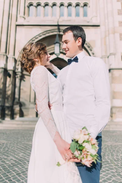 Sonriente pareja de recién casados bailando y abrazándose cerca de la antigua catedral cristiana gótica —  Fotos de Stock