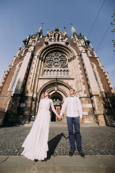 Romantyczna para newlywed valentynes pozowanie gospodarstwa ręce w pobliżu stary gotycki kościół — Zdjęcie stockowe