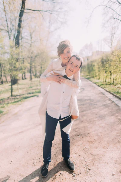 Damat gülümseyen güzel sarışın gelini arka açık havada bahar parkta taşır