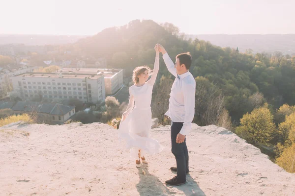 Porträtt av leende dansande bröllopspar på toppen kulle, stad och himmel bakgrund — Stockfoto