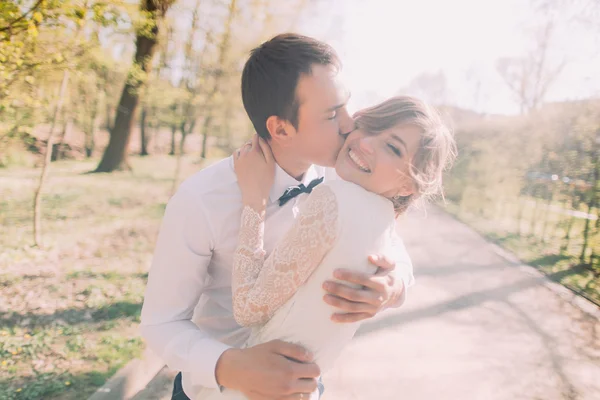 Молодой жених целует прекрасную невесту в щеку в весеннем парке — стоковое фото