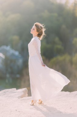 Akan beyaz elbise ile doğanın tepenin tepesinde duran güzel gülümseyen genç sarışın gelin