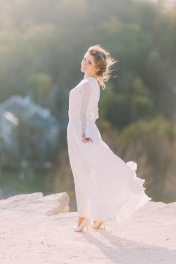 Akan beyaz elbise ile doğanın tepenin tepesinde duran güzel gülümseyen genç sarışın gelin