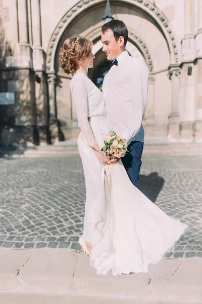 Smiling newlywed couple dancing and hugging near old gothic christian cathedral