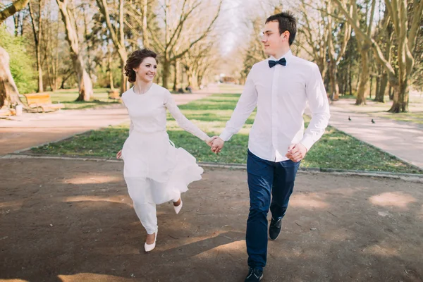 Gelukkige bruiloft paar charmante bruidegom en blonde bruid lopen met de hand op City Park Road — Stockfoto