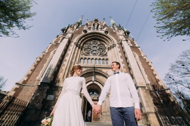 Romantik Çift, yeni evli valentynes holding poz yanında eski Gotik kilise eller.