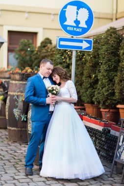 Gül buketi ve mavi elbiseli işareti öpücük yer altında kucaklayan yakışıklı damat ile gülümseyen güzel gelin