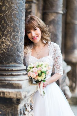 Gülümseyen gelin düğün buket sütunlarla, eski bina arka plan üzerinde tutarak yakın çekim