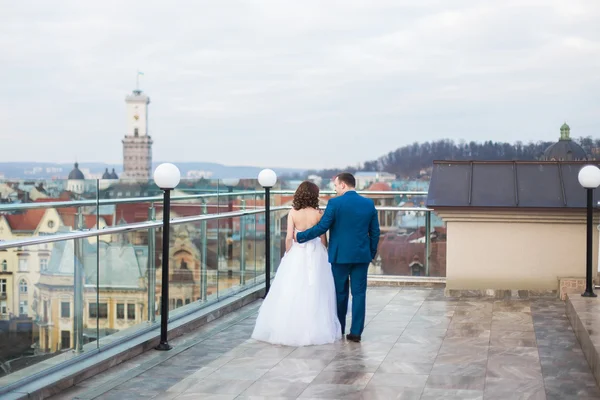 Hübsche Braut und brünetter Bräutigam gehen zurück auf die Terrasse mit Stadtbild Hintergrund — Stockfoto