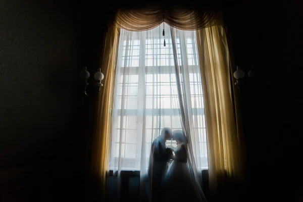 Silueta de novia y novio besándose contra la ventana con cortinas —  Fotos de Stock