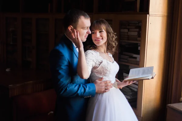 Söt brud och brudgum embracing witn bok nära fönster på gamla biblioteket — Stockfoto