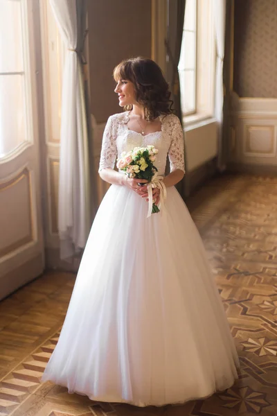 Visão de comprimento total da bela mulher posando em vestido de noiva perto da janela no interior de luxo — Fotografia de Stock