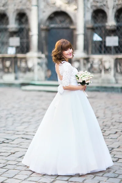 Молодая улыбающаяся невеста, позирующая с букетом роз, городской пейзаж на фоне — стоковое фото