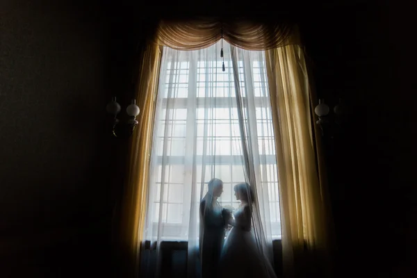 Gelin ve damat holding buket perdeler ile cama kucaklayan silüeti — Stok fotoğraf