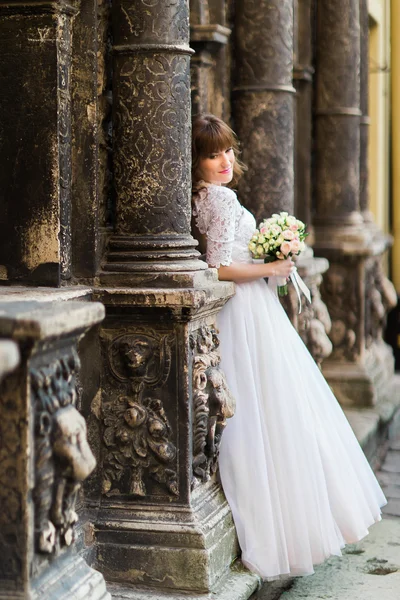 Bela noiva olhando para entre as colunas do antigo edifício e segurando buquê de noiva — Fotografia de Stock