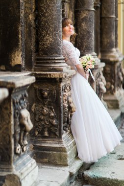 Güzel genç gelin doğru eski bina ve gelin buketi tutan sütunlar arasında seyir