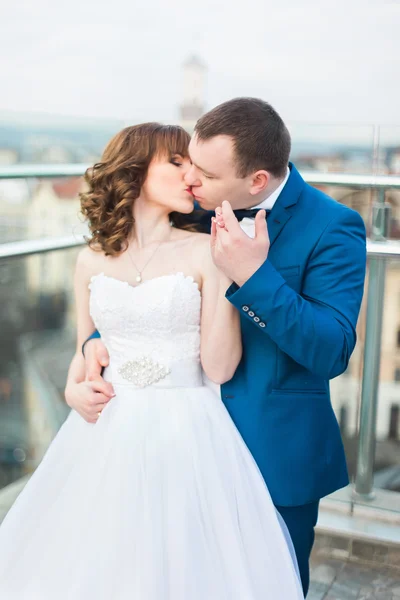 Noivo abraçando de volta noiva e beijando de pé no terraço com grande paisagem urbana — Fotografia de Stock