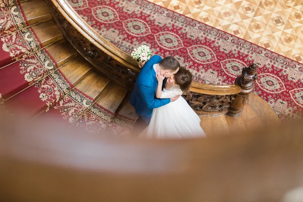 Beau marié élégant embrassant la joue de belle mariée souriante sur de vieux escaliers en bois au riche fond intérieur — Photo