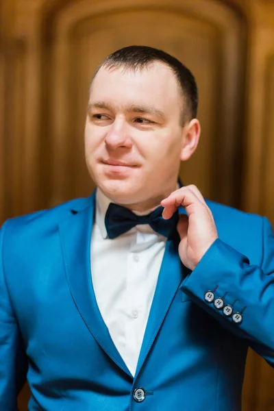 Красивий усміхнений чоловік у синьому костюмі зафіксував свою краватку в багатому дерев'яному інтер'єрі — стокове фото