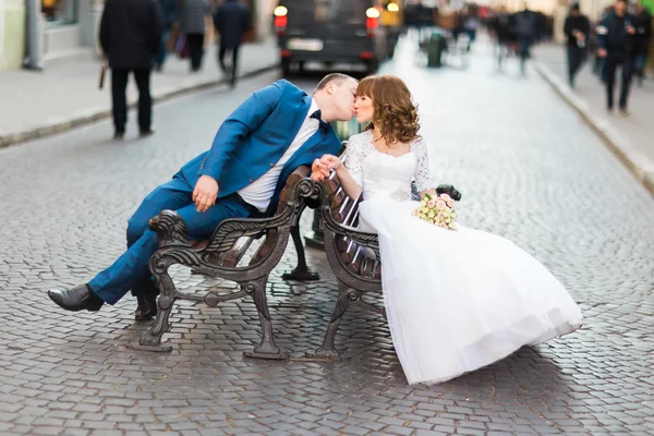 Romantické novomanželů, líbání a sedí na dřevěné lavici ve starém městě — Stock fotografie