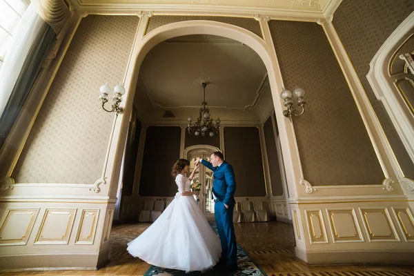 Bela noiva com buquê e belo noivo vestindo terno azul dançando em arco no fundo das paredes amarelas — Fotografia de Stock
