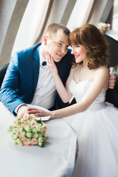 Linda noiva de cabelo castanho feliz tocando rosto de noivo elegante em terno azul sentado no restaurante — Fotografia de Stock