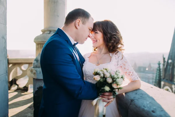 Mjuka vackra bruden och brudgummen håller hand embracing ansikte mot ansikte på gamla balkongen, bakgrunden stadsbild — Stockfoto
