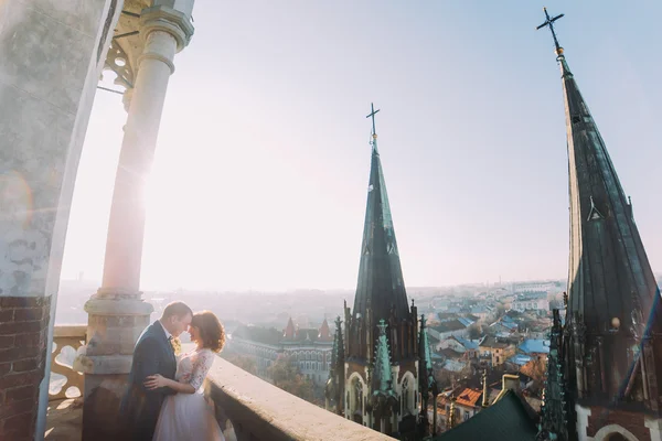 Zachte mooie bruid en bruidegom hand in hand omarmen face-to-face op het oude balkon, achtergrond stadsgezicht — Stockfoto