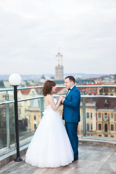 Чарівна весільна пара тримає руки на терасі з великим міським пейзажем — стокове фото