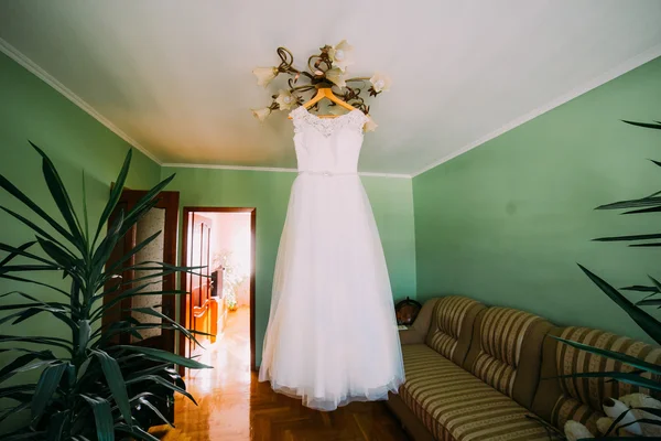 Vestido de noiva branco elegante pendurado no brilho no quarto do hotel decorado com plantas exóticas — Fotografia de Stock