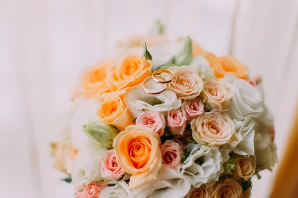 Buquê de noiva feito de rosas brancas, rosa e laranja com duas alianças de casamento em cima. Close-up — Fotografia de Stock