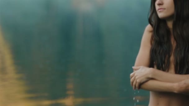 ノーメイクと長い黒髪を持つ若くて美しいセクシーな女の子のクローズアップは、背景に山シネビル湖のきれいな青い水で彼女の肌に柔らかく触れます。カルパチア山脈 — ストック動画