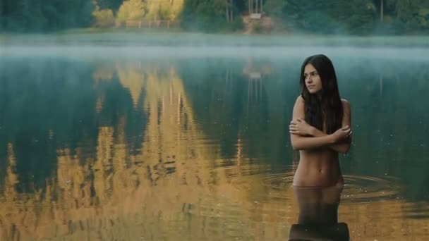 Primer plano de joven y hermosa sirena chica seductora sin maquillaje y pelo largo y oscuro tocando suavemente su piel con vista al lago de montaña Synevir en el fondo. Montañas Cárpatas — Vídeos de Stock