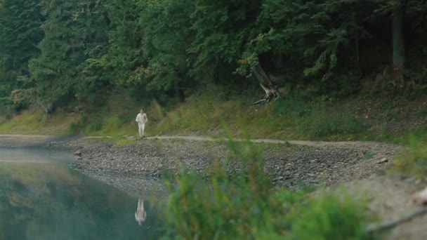 Schöner junger Mann in traditioneller Stickkleidung, der allein am felsigen Ufer des malerischen Bergsees Synevir in den Karpaten spaziert — Stockvideo