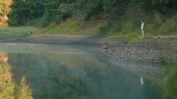 Gutaussehender junger Mann in traditioneller Stickkleidung blickt nachdenklich auf den malerischen Bergsee Synevir in den Karpaten. Konzept der Märchenmythologie — Stockvideo