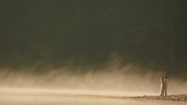 Glückliches Landpaar in ukrainischer ethnischer Kleidung, das sich bei Sonnenuntergang im goldenen Nebel am malerischen Bergsee in den Karpaten küsst. ewige Harmonie zwischen Mensch und Natur — Stockvideo