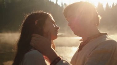 Ukrayna etnik giysiler içinde mutlu genç kırsal çift yakın şefkatle Karpatlar pitoresk dağ gölünde altın sis gün batımında güneş ışınları tarafından aydınlatılmış kucaklayan.