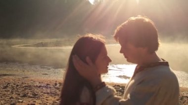Young man in ebroidery shirt softly embraces beautiful brunette woman on background of picturesque Synevir lake in Carpathian mountains. Wonderful sunset