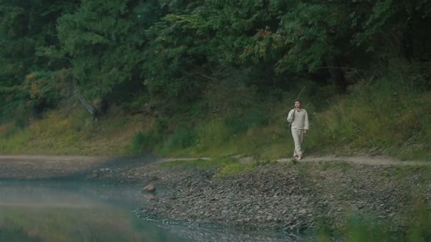 Handsome young mountain farmer in traditional embroidery clothes walking alone  on the rocky shore at the picturesque mountain lake Synevir in Carpathians — Stock Video