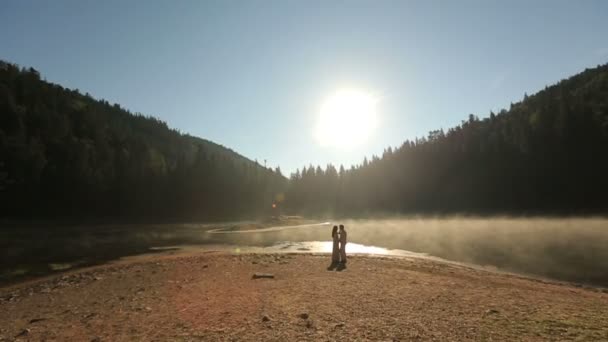 Hermosa joven feliz pareja enamorada en ropa bordada tradicional ucraniana en el pintoresco lago de montaña Synevir en Cárpatos. Atardecer dorado de verano en montañas — Vídeos de Stock