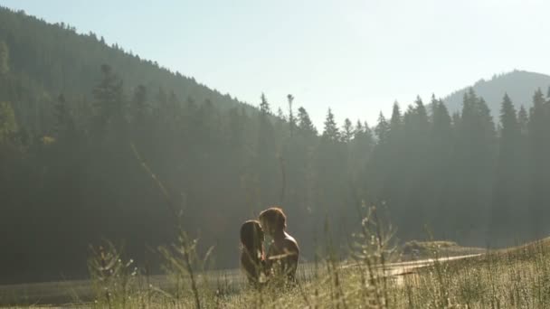 Happy together. Gorgeous young naked couple in love holding each other and kissing in a green field in mountains. Majestic mountains on background — Stockvideo